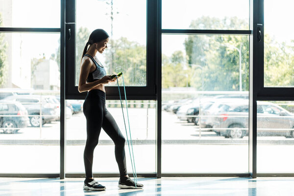 side view of happy young woman exercising with skipping rope 
