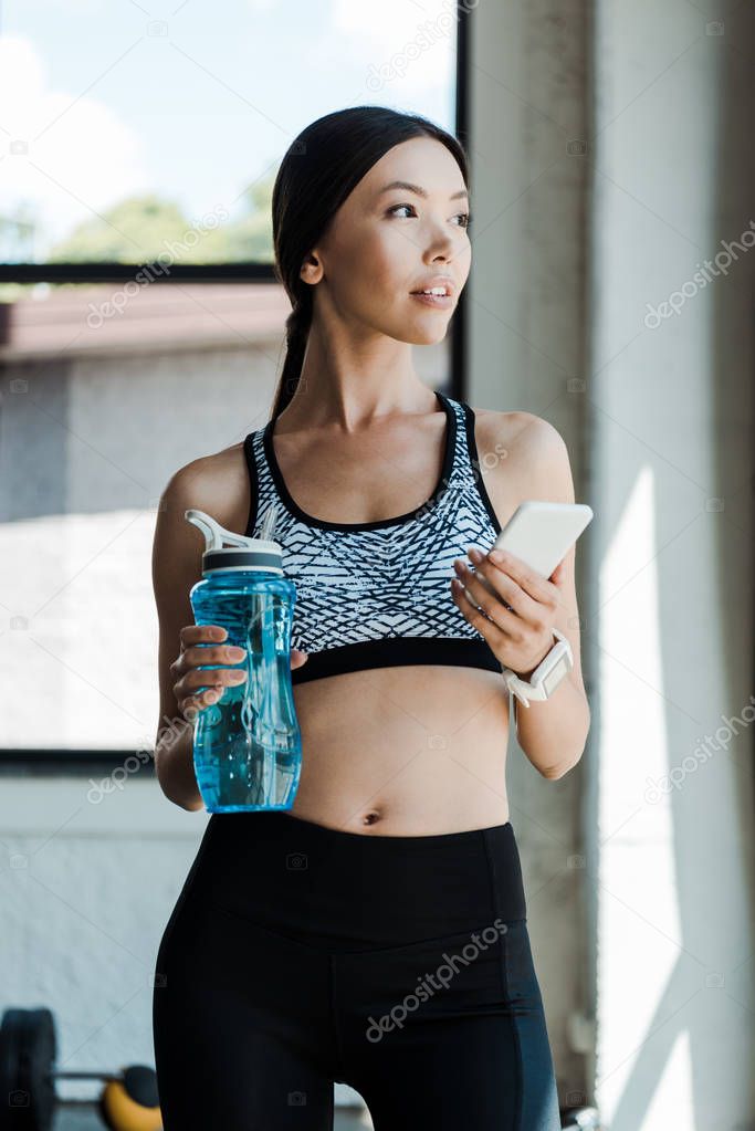 attractive woman using smartphone and holding sport bottle 