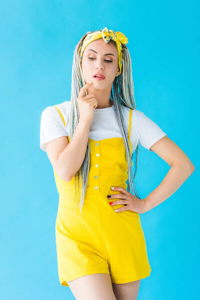 pensive girl with dreadlocks and finger on chin isolated on turquoise