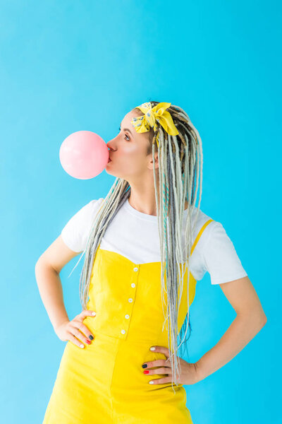 girl with dreadlocks and hands on hips blowing bubblegum isolated on turquoise