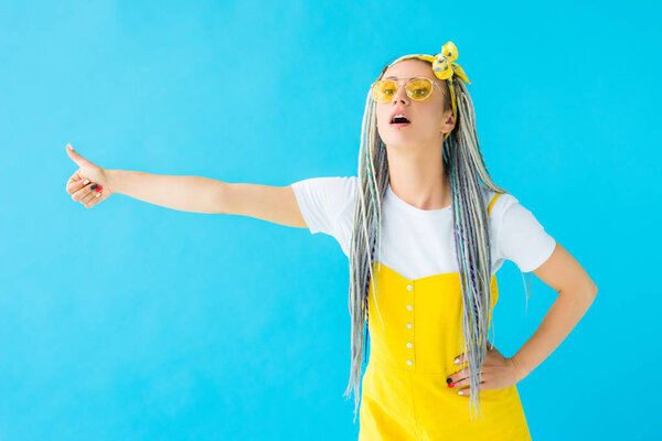 girl with dreadlocks in sunglasses showing thumb up isolated on turquoise