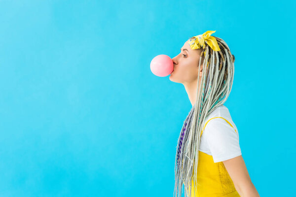 side view of girl with dreadlocks blowing bubblegum isolated on turquoise with copy space