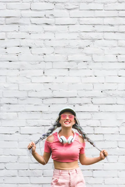 Hermosa Chica Sonriente Sombrero Con Auriculares Posando Cerca Pared Ladrillo —  Fotos de Stock