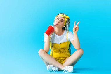 dreadlocks oturan güzel kız, barış işareti gösteren ve turkuaz üzerinde soda içme