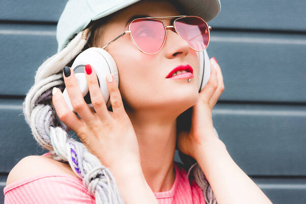 beautiful stylish girl with dreadlocks in sunglasses with hands on headphones