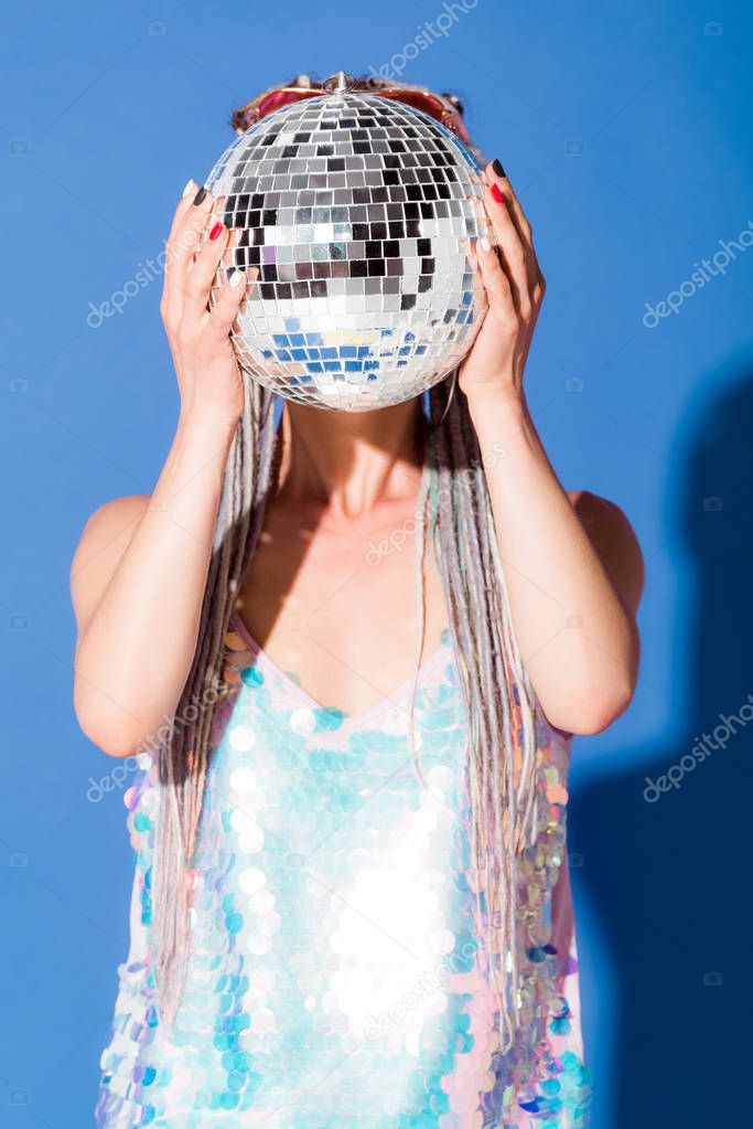 stylish girl covering face with disco ball on blue 