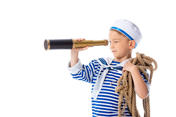 focused preschooler child in sailor costume looking in spyglass and holding rope isolated on white