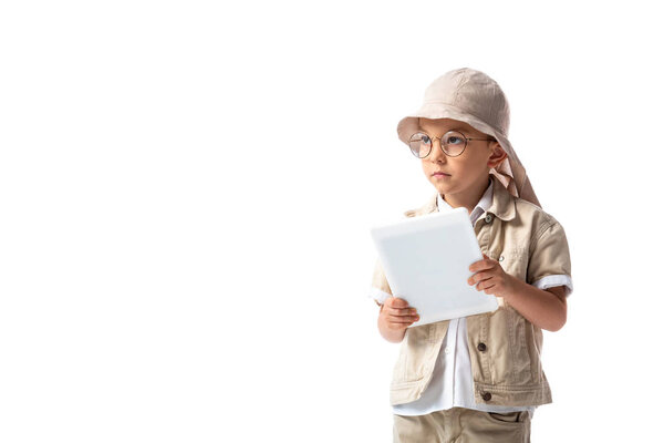pensive explorer child in glasses and hat holding digital tablet and looking away isolated on white