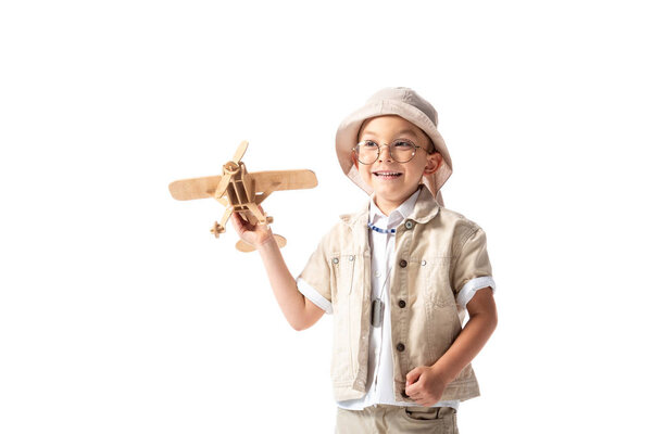 smiling explorer boy in glasses and hat holding wooden toy plane isolated on white
