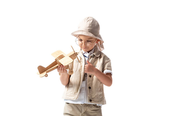 dreamy explorer boy in glasses and hat holding wooden toy plane isolated on white