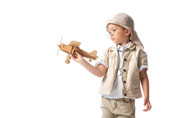 dreamy explorer boy in glasses and hat holding wooden toy plane isolated on white