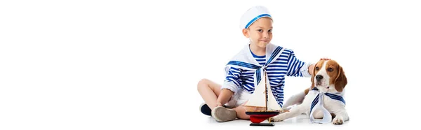 全景拍摄的微笑的男孩在水手西装与玩具船抚摸猎犬狗在白色 — 图库照片