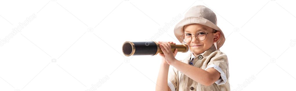 panoramic shot of smiling explorer boy in hat and glasses holding spyglass isolated on white