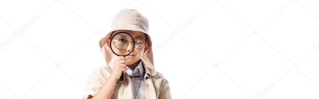 panoramic shot of curious explorer boy in hat looking through magnifier isolated on white