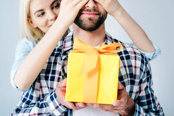 Hermosa Chica Cubriendo Ojos Hombre Celebración Presente Aislado Gris —  Fotos de Stock