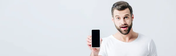 灰色で隔離された空白の画面でスマートフォンを示すショックを受けた男のパノラマショット — ストック写真