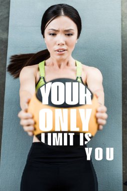 selective focus of girl holding ball while lying on fitness mat near your only limit is you letters  clipart