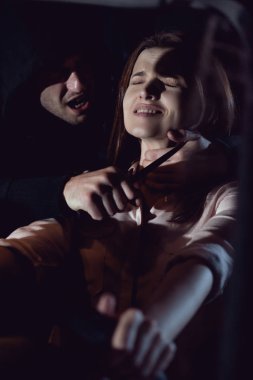 thief strangling beautiful frightened woman in automobile at night with knife clipart