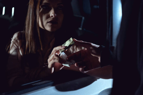 cropped view of woman in automobile with dollar banknotes buying drugs from thug 