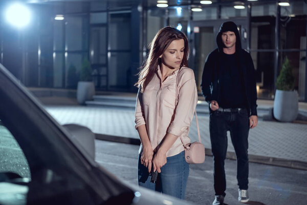 woman with gun near thief at night in parking lot