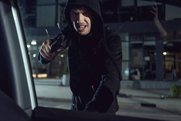 агрессивный вор в черной толстовке, направленный пистолет на окно машины
 