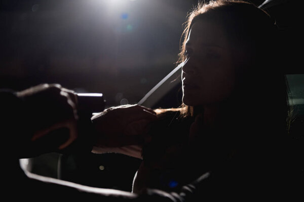 thief pointing gun at woman sitting in car at night with back light