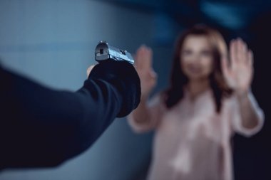 soyguncunun seçici odağı, yükseltilmiş ellere sahip kadına işaret tabancası