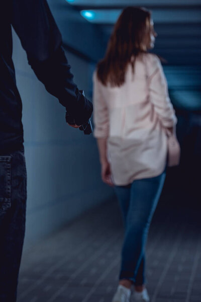 robber holding gun behind walking woman in underpass