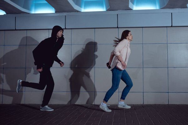 woman running away from thief in hoodie in underpass