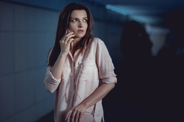 frightened beautiful woman talking on smartphone in underpass