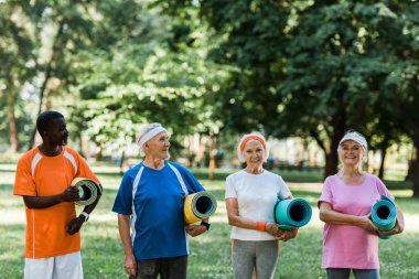 mutlu emekli ve çok kültürlü emekliler parkta fitness paspaslar tutan 