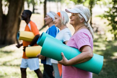 spor giyim çok kültürlü emekliler yakın fitness mat tutan mutlu emekli kadın seçici odak 