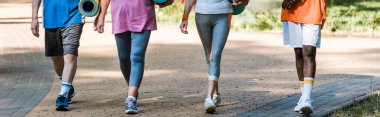 panoramic shot of senior and multicultural pensioners holding fitness mats and walking in park  clipart