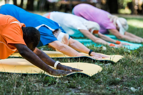 多元文化养老金领取者在公园健身垫上伸展的选择性焦点 — 图库照片