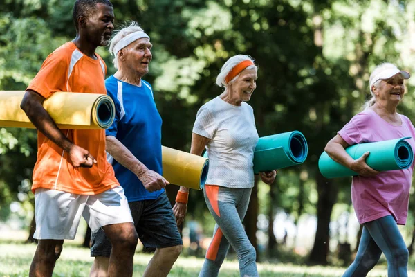 Nyugdíjas Többnemzetiségű Nyugdíjasok Szelektív Fókusza Parkban Sétálva Fitness Matracokat Tartva — Stock Fotó