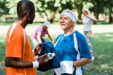 mutlu ve sportif üst düzey adam su ile şişe tutan ve Afrikalı Amerikalı adam bakarak seçici odak