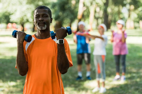 parkta egzersiz yaparken dumbbells tutan üst düzey afro-amerikan adam seçici odak 