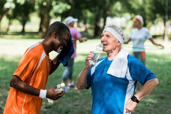 运动型多元文化的选择性焦点 退休男性拿着瓶子与水接近高级妇女 — 图库照片