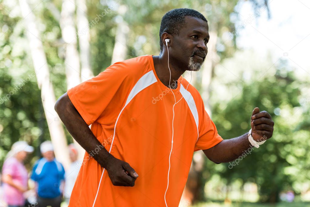 selective focus of senior african american man running and listening music in earphones 