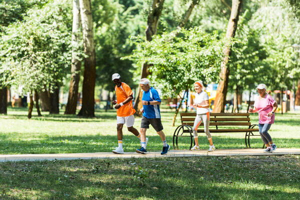 Мультикультурные и пожилые мужчины и женщины в спортивной одежде бегают в зеленом парке
 