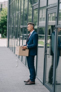 karton kutuda retro telefon ile binanın yanında duran takım elbiseli adam yan görünümü 