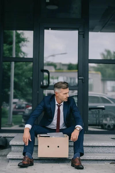 カートンボックスの近くの階段に座ってスーツを着て解雇されたビジネスマン — ストック写真