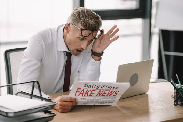 フェイクニュースで新聞を読みながら眼鏡に触れる感情的なビジネスマンの選択的な焦点 — ストック写真