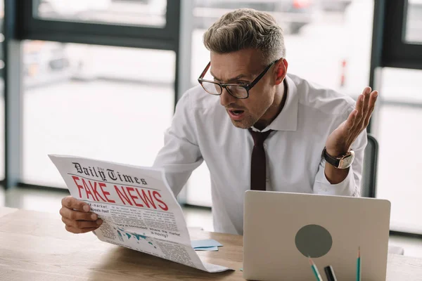 眼鏡でショックを受けたビジネスマンは 偽のニュースで新聞をジェスチャーし 読んでいます — ストック写真