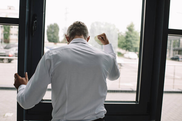 back view of businessman standing with clenched fist near windows