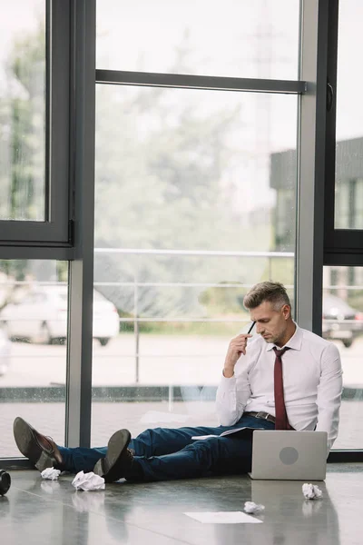 Hombre Guapo Sosteniendo Pluma Mientras Está Sentado Suelo Cerca Computadora — Foto de Stock