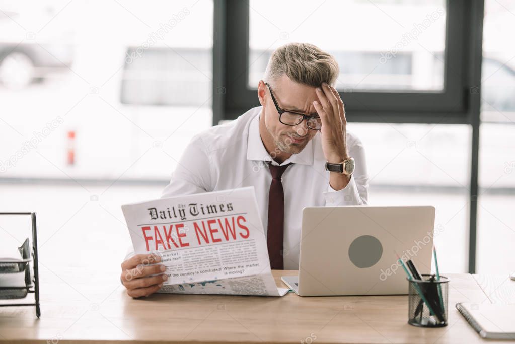 upset businessman in glasses holding newspaper with fake news 