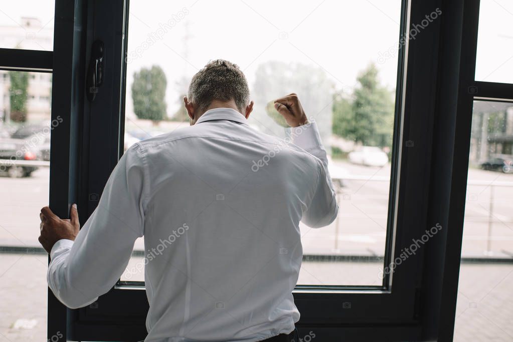 back view of businessman standing with clenched fist near windows