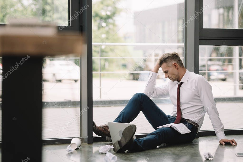 selective focus of man touching hair while sitting on floor near windows 