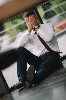 yerde otururken elleri ile yüz kaplayan üzgün adamın seçici odak 